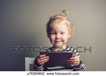 Stock Image - Toddler holding up digital tablet, grey background. Fotosearch