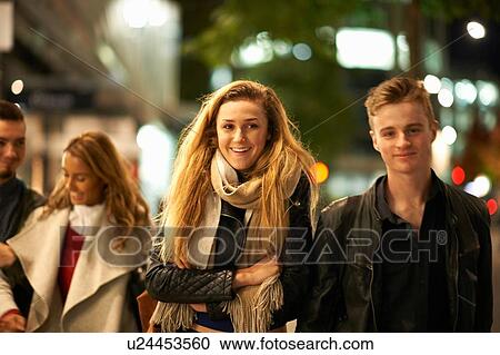 Stock Image - Two young couples strolling arm in arm along street at night, London, UK. Fotosearch
