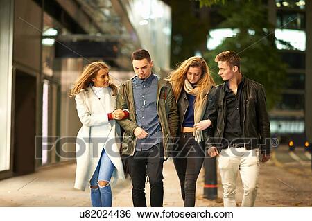 Two young couples strolling arm in arm on street at night, London, UK View Large Photo Image Stock Photograph - Two young couples strolling arm in arm on street at night, London, UK. Fotosearch