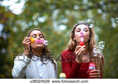 Two young female friends blowing bubbles in park View Large Photo Image Stock Photo - Two young female friends blowing bubbles in park. Fotosearch