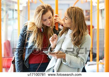 Two young female friends on train, looking at smartphone View Large Photo Image Stock Image - Two young female friends on train, looking at smartphone. Fotosearch