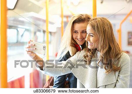 Two young female friends on train, taking self portrait, using smartphone View Large Photo Image Stock Photo - Two young female friends on train, taking self portrait, using smartphone. Fotosearch