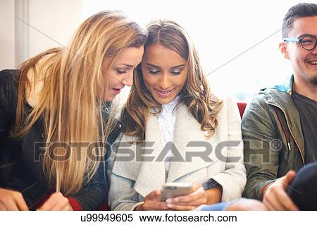 Two young female friends on train, looking at smartphone View Large Photo Image Stock Photography - Two young female friends on train, looking at smartphone. Fotosearch