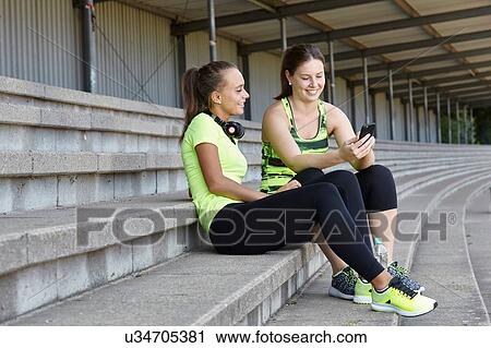 Two young female runners chatting in stadium seating View Large Photo Image Stock Image - Two young female runners chatting in stadium seating. Fotosearch