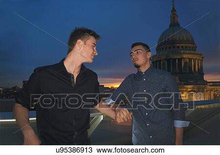Stock Image - Two young men holding hands in front of St Pauls at night, London, UK. Fotosearch