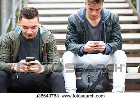 Two young men, sitting on steps, using smartphones, outdoors View Large Photo Image Stock Image - Two young men, sitting on steps, using smartphones, outdoors. Fotosearch