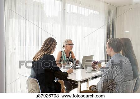 Stock Photo - View through window of colleagues sitting at table having business breakfast meeting. Fotosearch