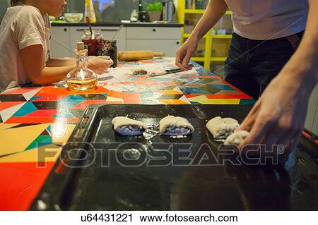 Woman and son placing pastry slices on baking tin at kitchen table View Large Photo Image Stock Image - Woman and son placing pastry slices on baking tin at kitchen table. Fotosearch