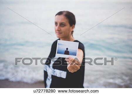 Woman holding up photograph of herself on beach View Large Photo Image Stock Image - Woman holding up photograph of herself on beach. Fotosearch