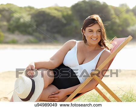 Stock Photo - Woman in swimsuit sitting on beach chair, Point Impossible, Victoria, Australia. Fotosearch