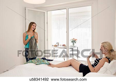Woman lying on bed holding coffee cup helping friend to choose outfit View Large Photo Image Stock Image - Woman lying on bed holding coffee cup helping friend to choose outfit. Fotosearch