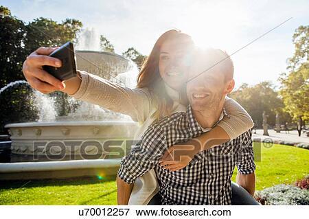 Woman taking selfie having a piggy back in park View Large Photo Image Stock Photo - Woman taking selfie having a piggy back in park. Fotosearch