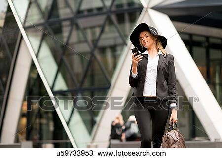 Stock Image - Woman texting while walking, 30 St Mary Axe in background, London, UK. Fotosearch