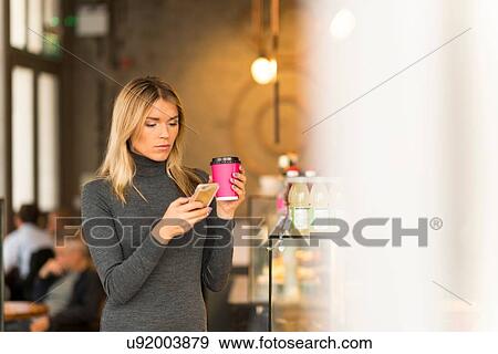 Stock Photo - Woman with takeaway coffee using smartphone. Fotosearch