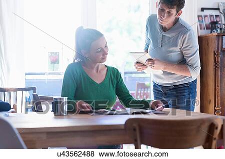 Stock Photo - Women in dining room sitting at table reading magazine. Fotosearch