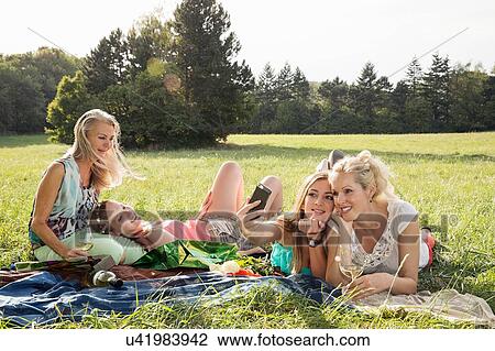 Women lying on fronts on grass using smartphone to take selfie smiling View Large Photo Image Stock Image - Women lying on fronts on grass using smartphone to take selfie smiling. Fotosearch