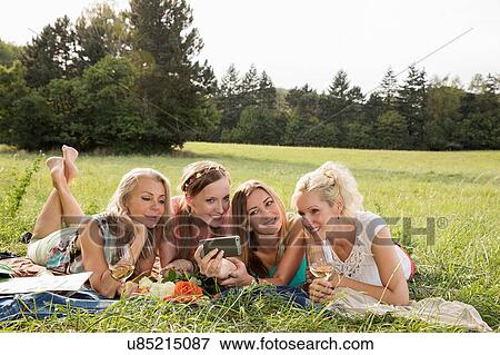 Women lying on fronts on grass using smartphone to take selfie smiling View Large Photo Image Stock Photo - Women lying on fronts on grass using smartphone to take selfie smiling. Fotosearch