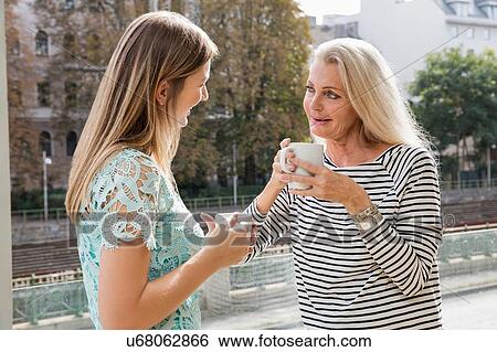Stock Photograph - Women outdoors holding coffee cups face to face smiling. Fotosearch