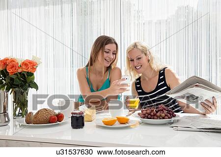 Women sitting at dining table enjoying a continental breakfast together, looking at cellular phone smiling View Large Photo Image Stock Image - Women sitting at dining table enjoying a continental breakfast together, looking at cellular phone smiling. Fotosearch