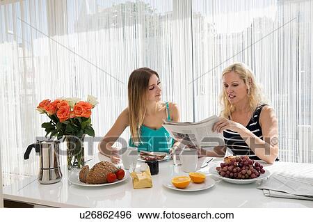 Women sitting at dining table enjoying a continental breakfast together, reading newspaper View Large Photo Image Stock Photograph - Women sitting at dining table enjoying a continental breakfast together, reading newspaper. Fotosearch