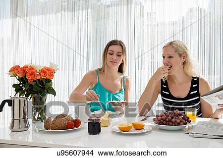 Women sitting at dining table spreading butter on bread, eating a continental breakfast together View Large Photo Image Picture - Women sitting at dining table spreading butter on bread, eating a continental breakfast together. Fotosearch