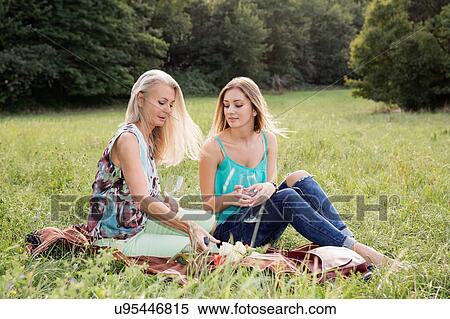 Women sitting on picnic blanket in park enjoying a glass of wine View Large Photo Image Stock Photography - Women sitting on picnic blanket in park enjoying a glass of wine. Fotosearch