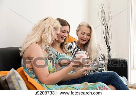 Women sitting on sofa holding coffee cups looking at photographs smiling View Large Photo Image Stock Image - Women sitting on sofa holding coffee cups looking at photographs smiling. Fotosearch