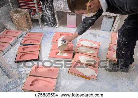 Picture - Worker casting plaster into foot moulds for orthopaedic support in factory. Fotosearch