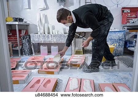 Picture - Worker casting plaster into foot moulds for orthopaedic support in factory. Fotosearch