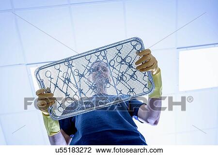 Stock Image - Worker with tray of surgical instruments in surgical instrument factory, low angle view. Fotosearch