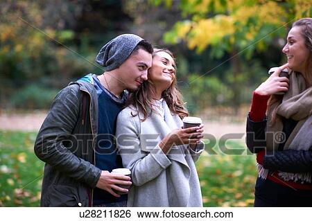 Stock Photograph - Young adult friends chatting and drinking takeaway coffee in autumn park. Fotosearch