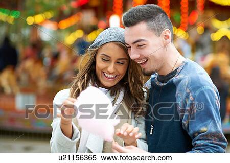 Stock Photography - Young couple eating candy floss at funfair, outdoors. Fotosearch