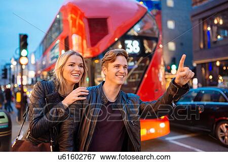 Stock Photo - Young couple hailing a taxi on city street at night, London, England, UK. Fotosearch