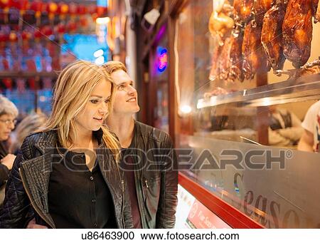 Stock Image - Young couple looking in restaurant window at night, Chinatown, London, England, UK. Fotosearch