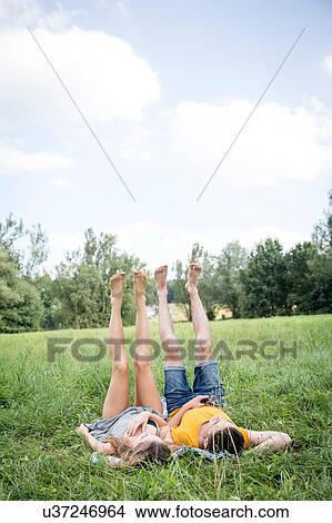 Young couple lying on grass in field, legs raised View Large Photo Image Picture - Young couple lying on grass in field, legs raised. Fotosearch
