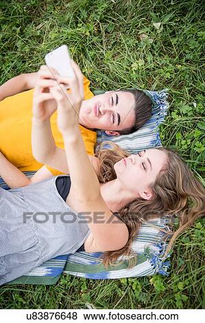 Young couple lying on grass in field, taking self portrait using smartphone View Large Photo Image Stock Photo - Young couple lying on grass in field, taking self portrait using smartphone. Fotosearch