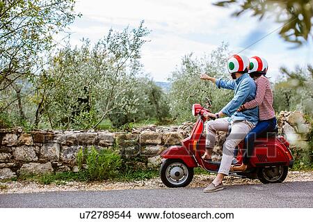 Picture - Young couple on moped pointing at olive grove, Florence, Italy. Fotosearch