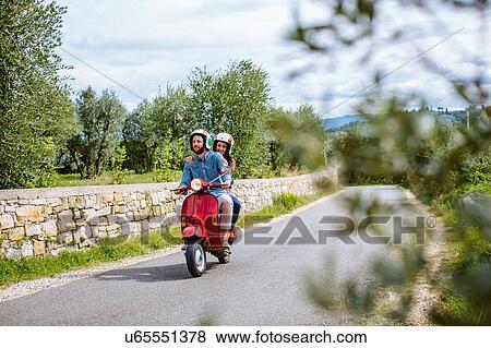 Stock Photo - Young couple riding moped past olive grove, Florence, Italy. Fotosearch