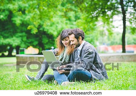 Young couple sitting cross legged on grass using laptop computer looking down smiling View Large Photo Image Stock Photo - Young couple sitting cross legged on grass using laptop computer looking down smiling. Fotosearch