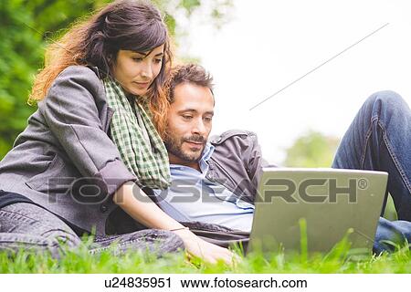 Young couple sitting on grass looking down using laptop computer View Large Photo Image Stock Image - Young couple sitting on grass looking down using laptop computer. Fotosearch