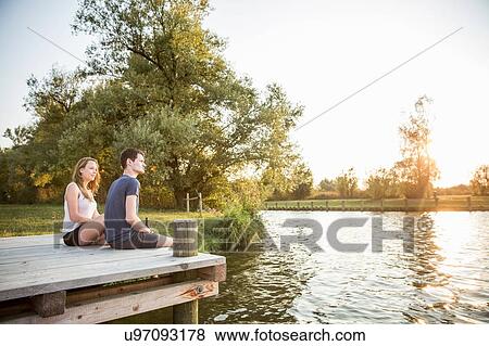 Stock Photo - Young couple sitting on jetty, relaxing. Fotosearch