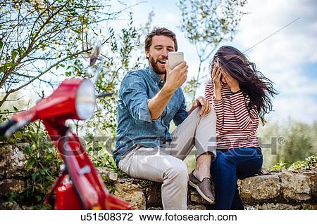 Young couple sitting on olive grove wall reading smartphone, Florence, Italy View Large Photo Image Stock Image - Young couple sitting on olive grove wall reading smartphone, Florence, Italy. Fotosearch