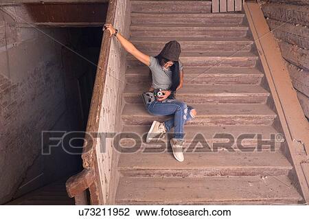 Stock Image - Young female photographer preparing camera on stairs in old industrial building. Fotosearch