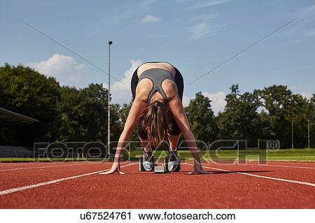 Young female runner bending forward on race track starting line View Large Photo Image Stock Image - Young female runner bending forward on race track starting line. Fotosearch