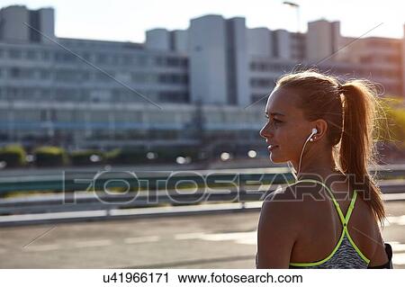 Young female runner listening to earphone music on urban rooftop View Large Photo Image Stock Image - Young female runner listening to earphone music on urban rooftop. Fotosearch