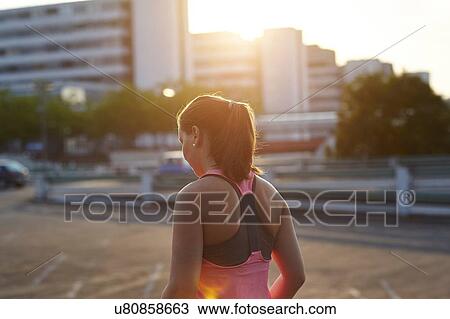 Stock Image - Young female runner on sunlit rooftop. Fotosearch