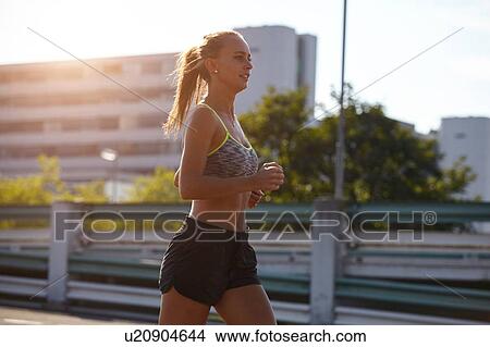 Picture - Young female runner running on urban rooftop. Fotosearch