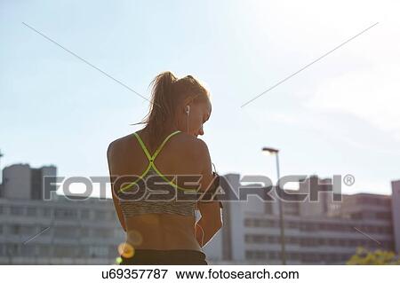 Stock Photo - Young female runner selecting music on urban rooftop. Fotosearch