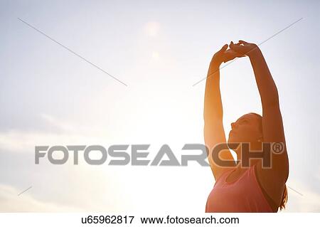 Young female runner stretching arms against sunlit sky View Large Photo Image Stock Photo - Young female runner stretching arms against sunlit sky. Fotosearch