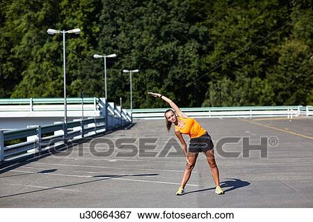 Young female runner stretching in parking lot View Large Photo Image Stock Photo - Young female runner stretching in parking lot. Fotosearch